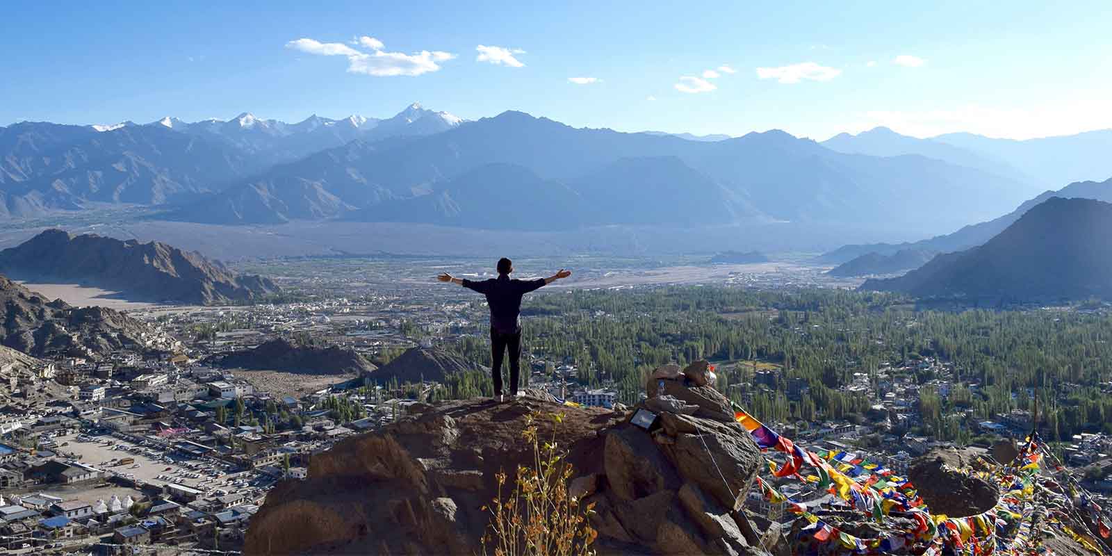 Trekker standing on summit overlooking Leh surrounded by Himalayas