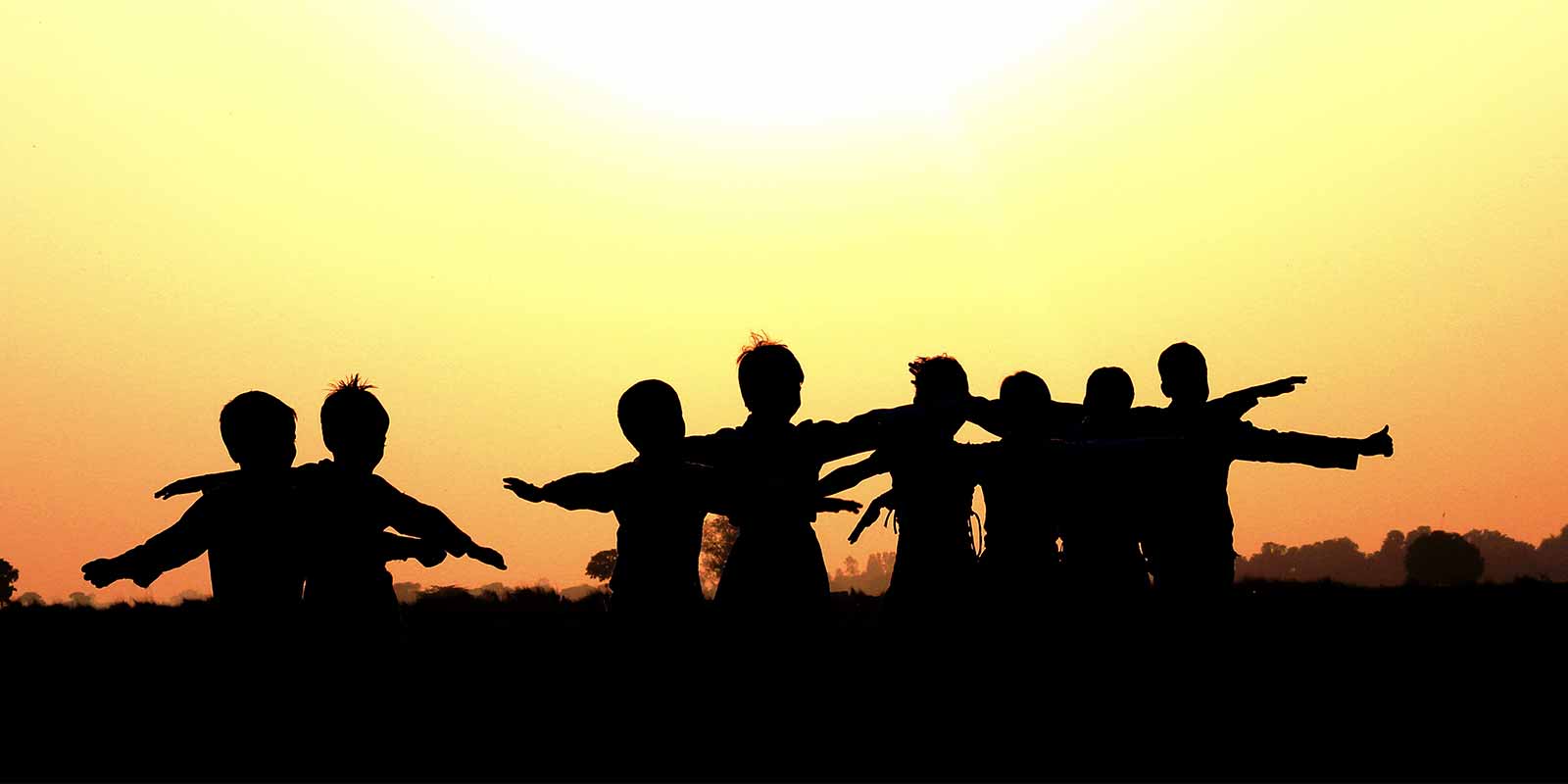 Silhouette of children with arms outstretched at sunset