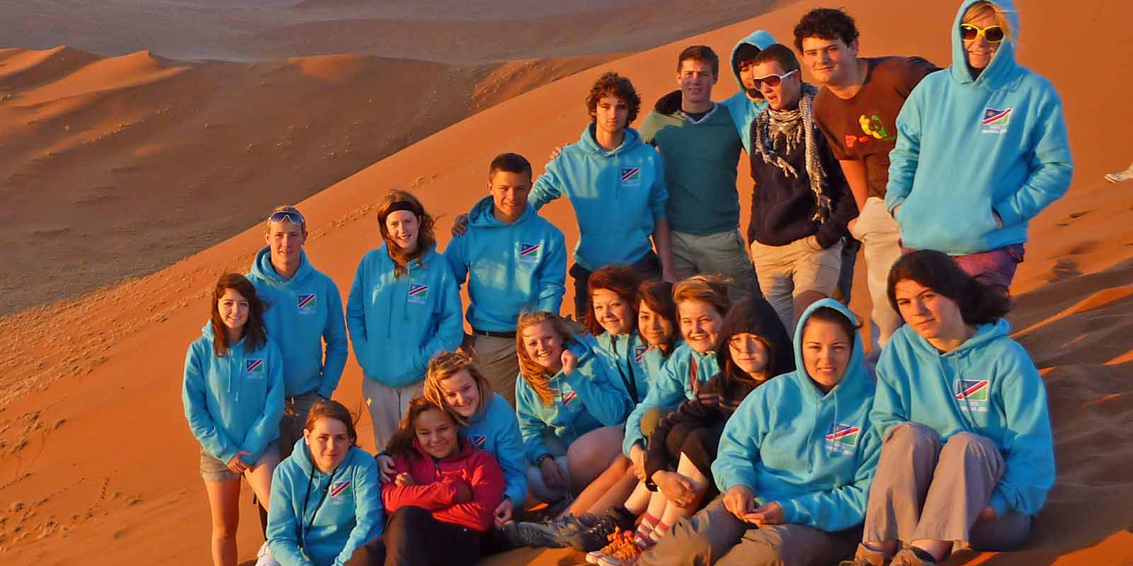 A group of students gathered at the top of a desert dune in the evening sun