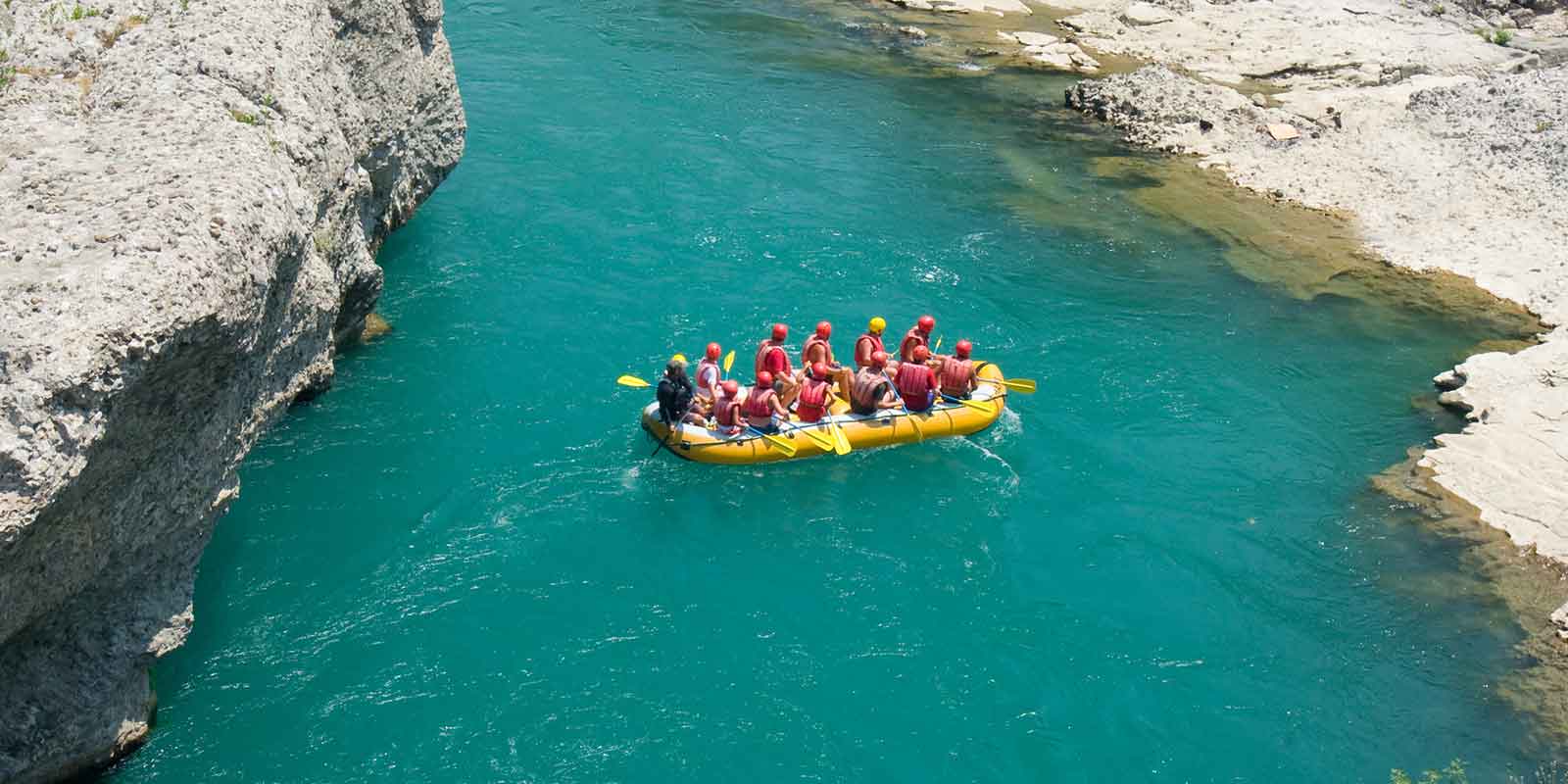 Aerial view of group rafting in a turquoise river with rocky cliffs either side