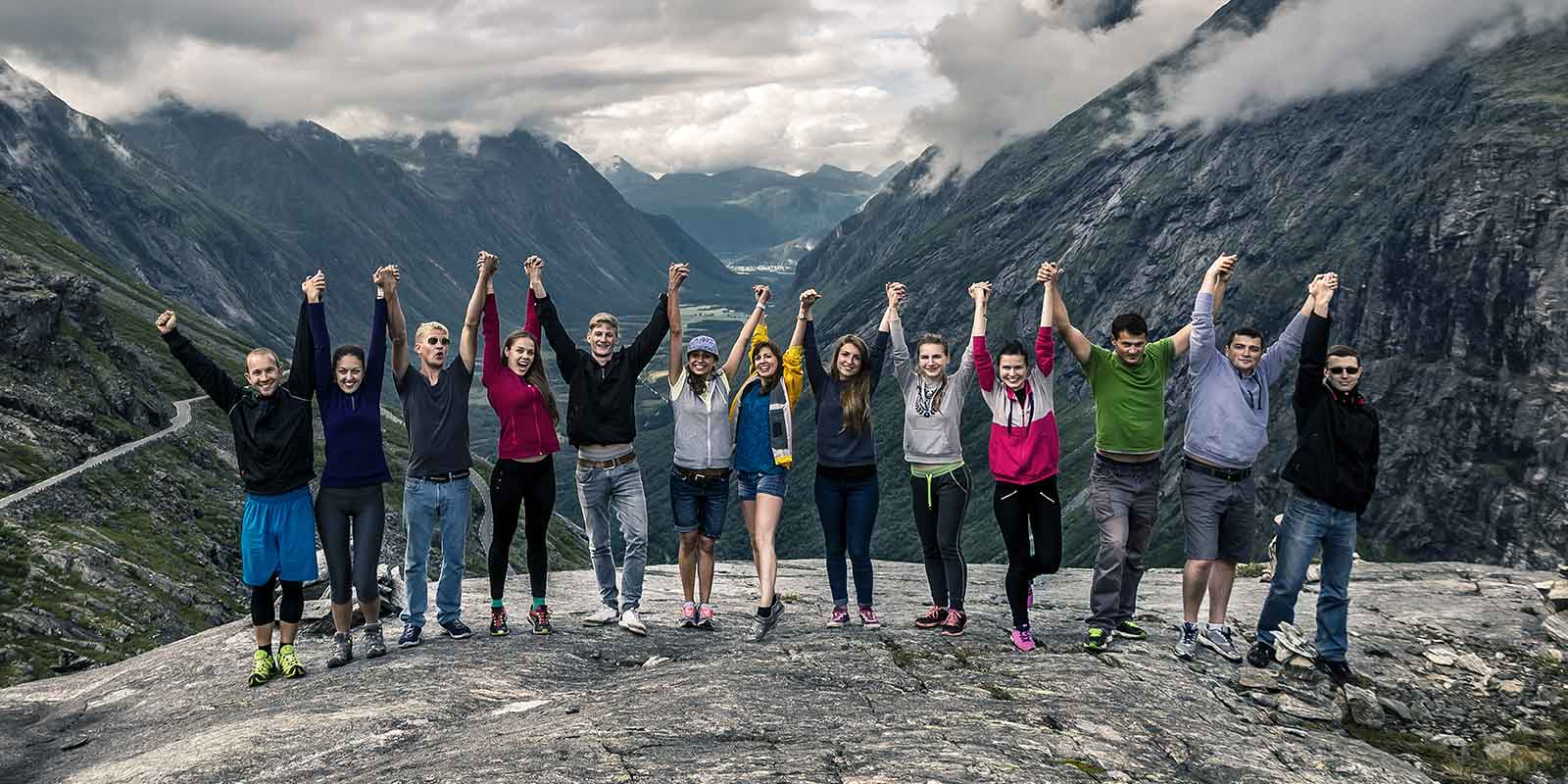 Group of young people joining hands in celebration in front of mountain range
