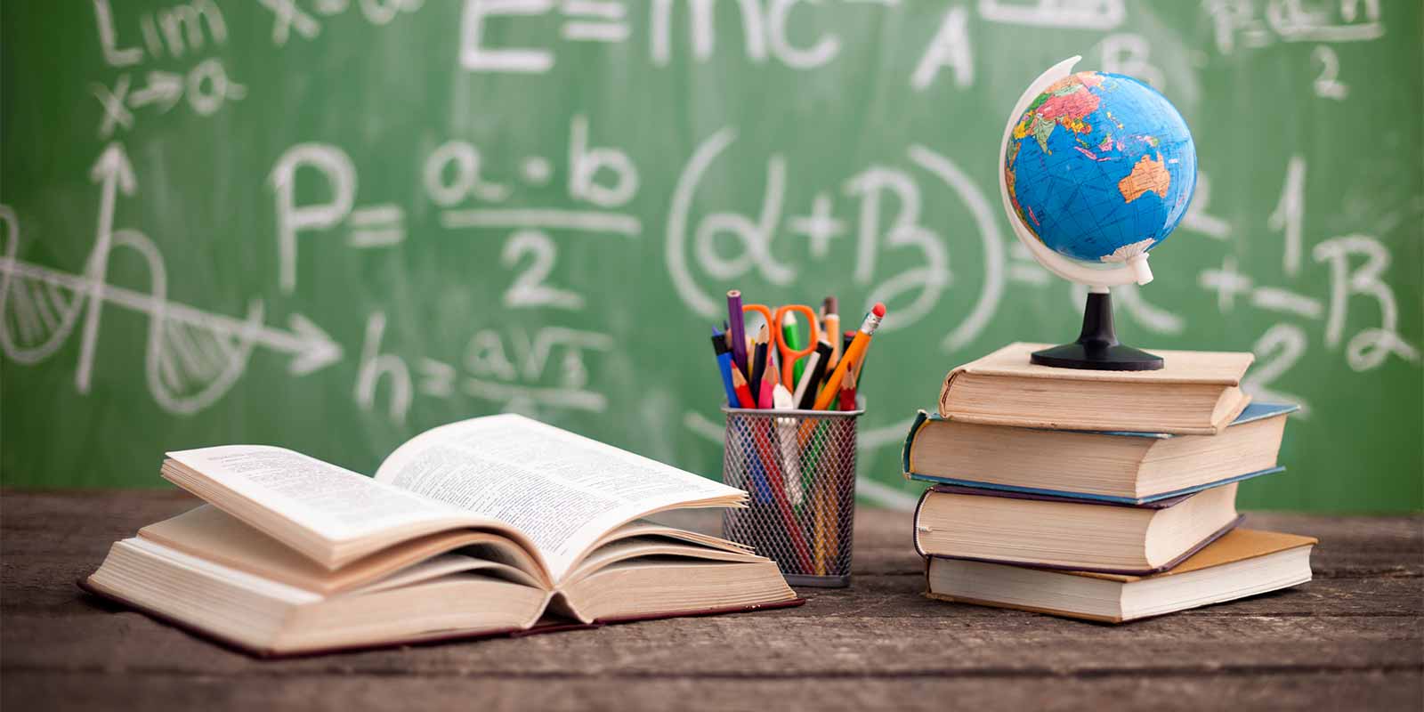School books with pens and globe in front of classroom blackboard