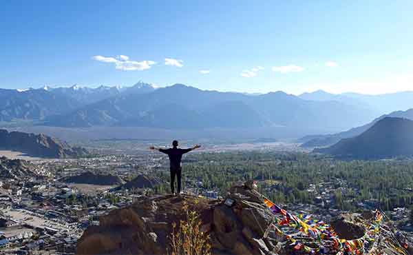 Trekker standing on summit overlooking Leh surrounded by Himalayas