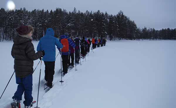 Group snowshoeing in Finland in a line with moon in the sky