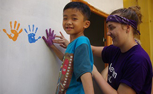 Student and local child painting hand prints on school building in Vietnam