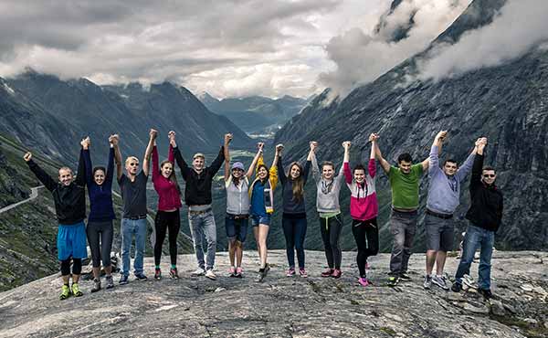 Group of young people joining hands in celebration in front of mountain range
